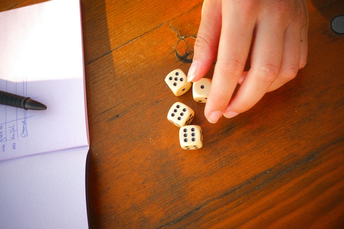 Une main pose quatre dés sur une table en bois, à côté d’un carnet.