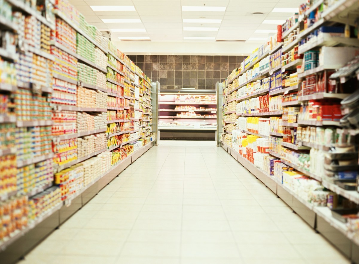Une allée de supermarché aux rayons pleins, vue en enfilade.