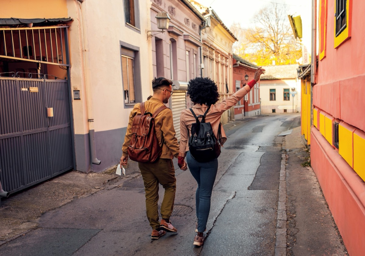 Un couple marche main dans la main dans une ruelle colorée, la femme lève le bras.