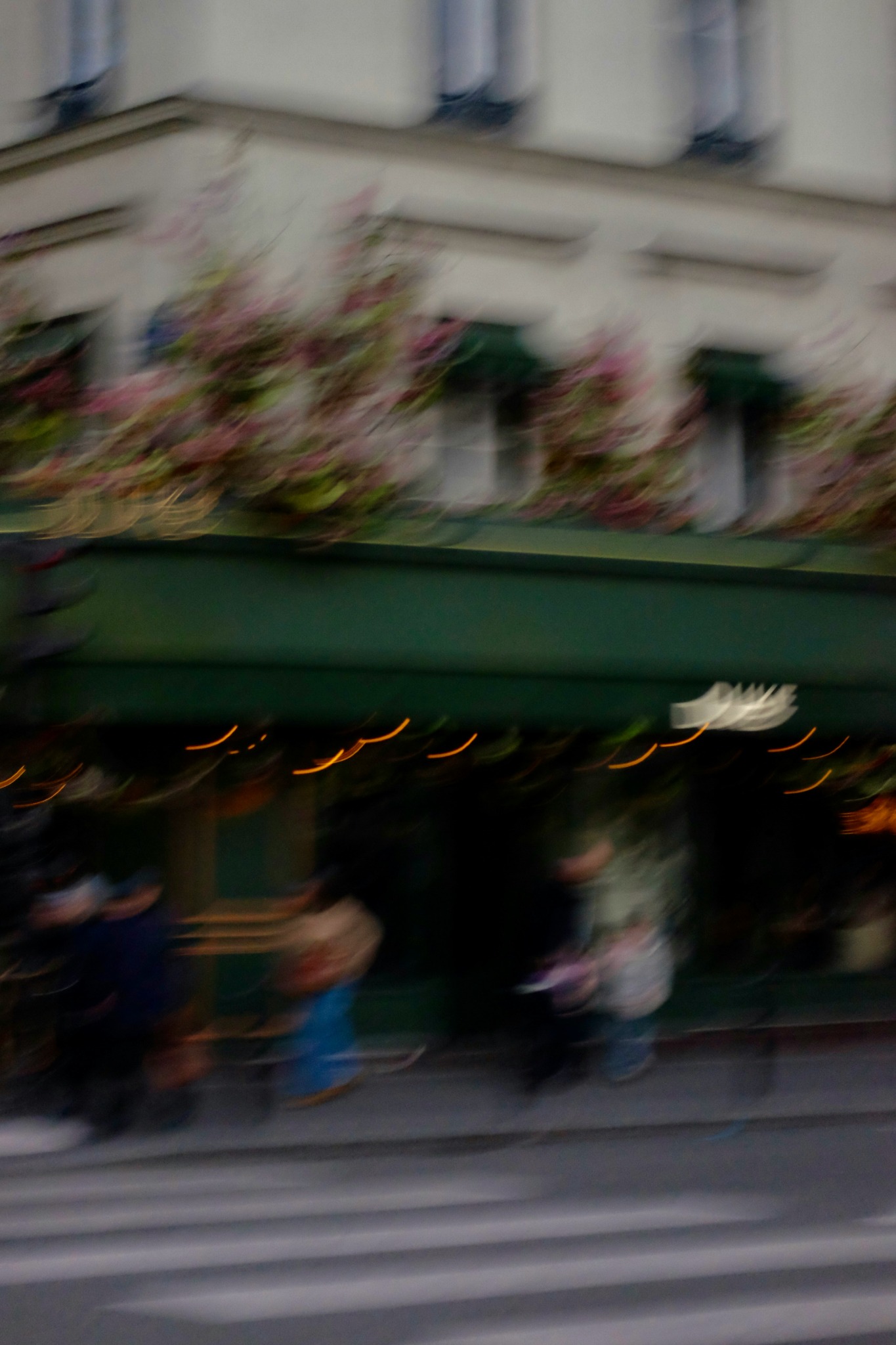 Passants devant un café parisien, photographiés dans un flou de mouvement.